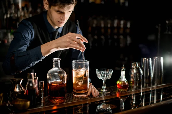 Young bartender gently stirs cold cocktail with spoon — Stok fotoğraf