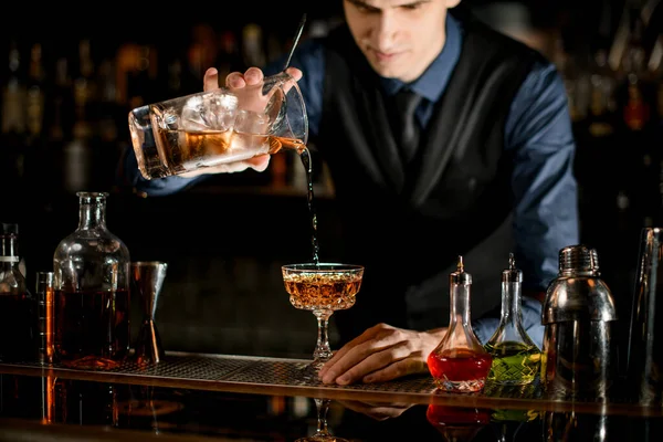 Young bartender pours a ready-made cold cocktail into wineglass. — Stockfoto