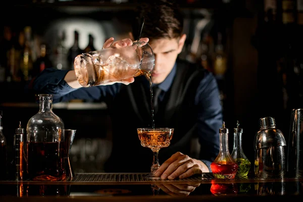 Young bartender gently pours brown cocktail into glass. — Stok fotoğraf