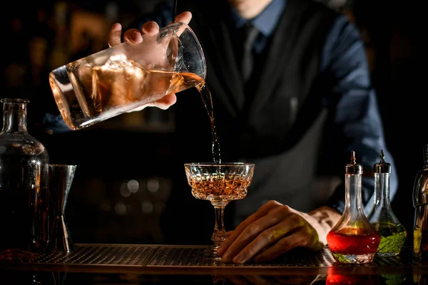 Close-up how bartender pours a ready-made cold brown cocktail into wineglass. — Stockfoto