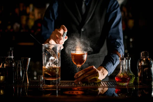 Cantinero espolvorea en un vaso con una bebida alcohólica marrón . — Foto de Stock
