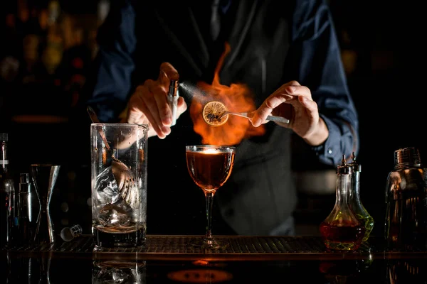 Professional man at the bar sprinkles burning slice of citrus for cocktail. — Stock fotografie