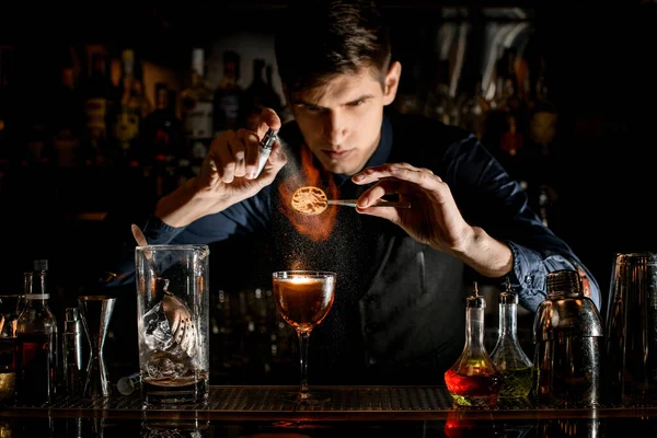 Professional barman at the bar sprinkles burning slice of citrus for cocktail. — Stok fotoğraf