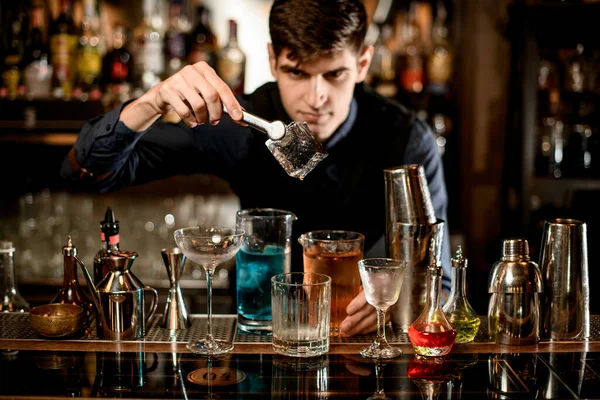 Barman segura por fórceps cubo de gelo grande sobre um copo no bar . — Fotografia de Stock