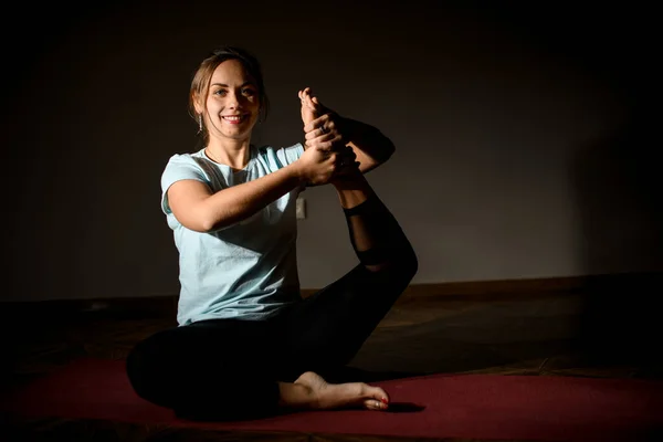 Ung leende flicka i studion på speciella röda golv mattor gör yoga pose. — Stockfoto