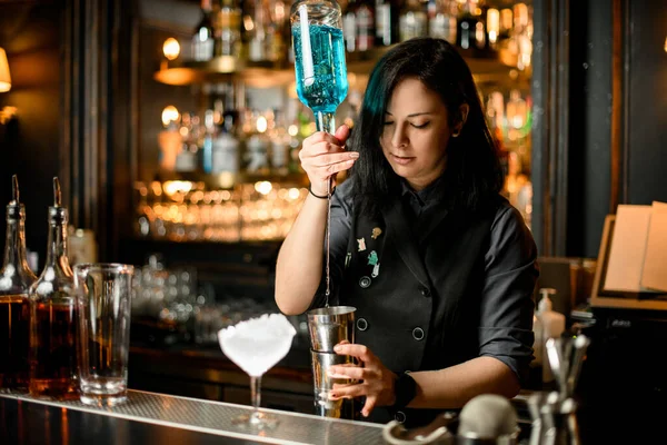Mulher barman derrama bebida alcoólica azul em shaker para fazer coquetel . — Fotografia de Stock
