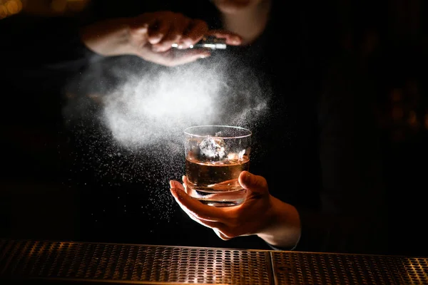 Professionelle Barkeeper hält in einer Hand Glas mit alkoholischen Getränken und streut darauf. — Stockfoto