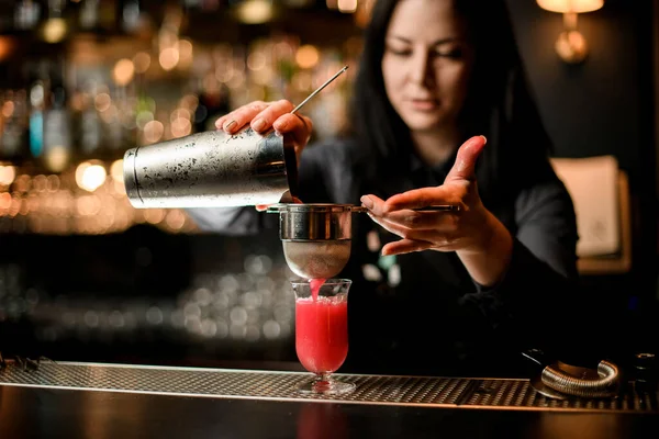 Bartender mulher profissionalmente derrama coquetel de shaker em vidro usando peneira . — Fotografia de Stock