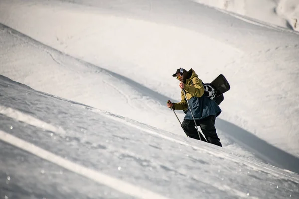 戴眼镜的男人带着滑雪器材和手杖爬上雪山 — 图库照片