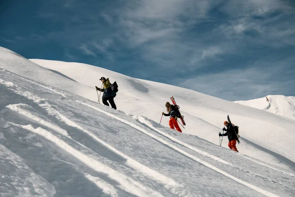 Três pessoas com equipamento de esqui e paus sobe montanha nevada . — Fotografia de Stock