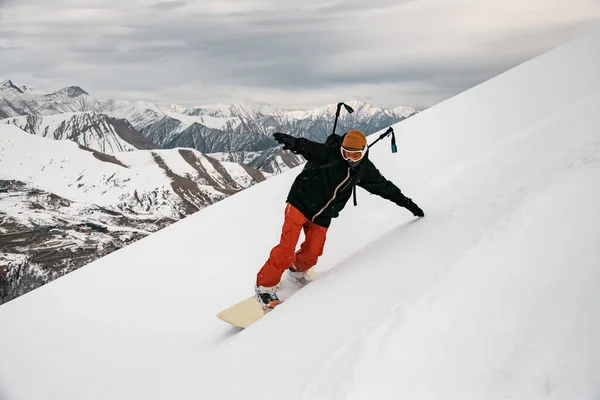 Homme snowboarder en vêtements lumineux descendant la montagne . — Photo