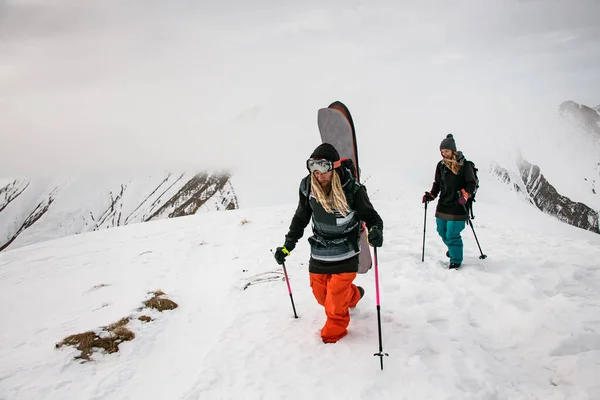 Два путешественника с сноубордами, взбирающиеся на гору — стоковое фото