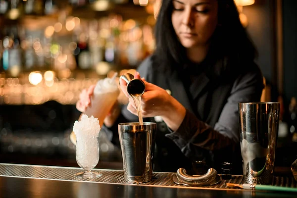 Morena barman gentilmente derrama a bebida em aço agitador usando copo — Fotografia de Stock