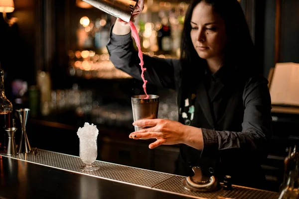 Brünetten Barmann professionell gießt Cocktail aus Stahl Shaker in Glas mit Sieb. — Stockfoto