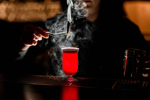 Barman utilizzando pinzette tiene bastone fumo sopra cocktail rosso brillante — Foto Stock
