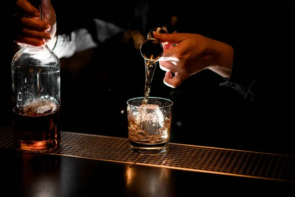 Bartender professionellt häller alkoholhaltig dryck till glas med is med hjälp av bägare. — Stockfoto