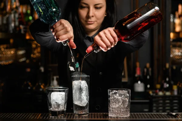 Barkeeperin gießt Getränk behutsam mit Eis aus Flasche in Glas. — Stockfoto