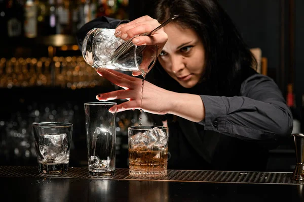Mulher barman muito cuidadosamente derrama bebida de um copo para outro . — Fotografia de Stock
