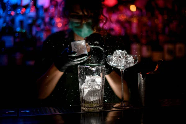 Close-up. Woman barman in medical mask and black gloves with special device breaks pieces of ice.