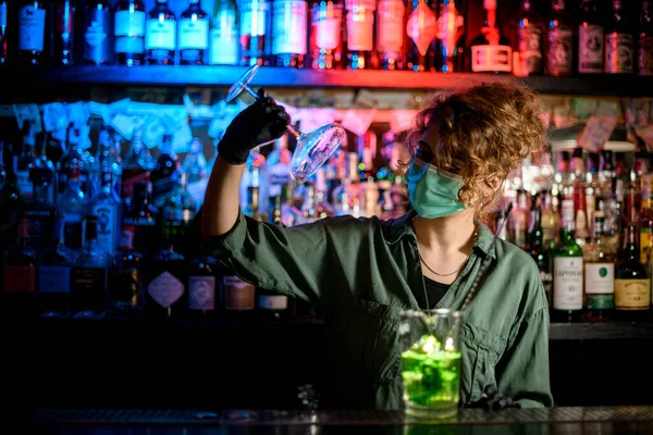 Chica joven en el mostrador de bar en máscara médica y guantes negros sostiene el vidrio . — Foto de Stock