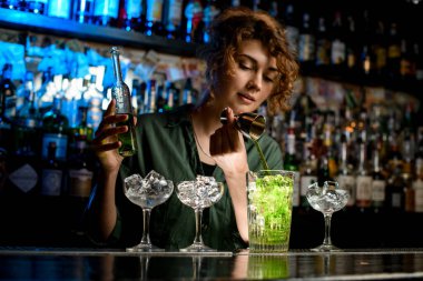 Genç bayan barmen dikkatli bir şekilde yeşil içeceği kullanılmış büyük bardağa doldurur..