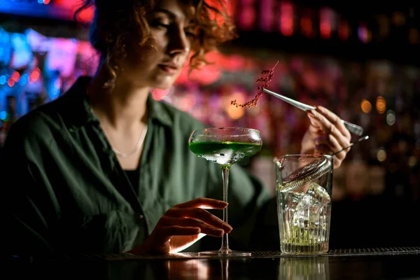 Молодая женщина бармен держит стекло с коктейлем и нежно украшает его — стоковое фото