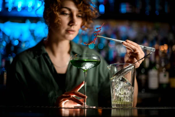 Mujer joven en el bar sostiene el vaso con cóctel y lo decora cuidadosamente — Foto de Stock