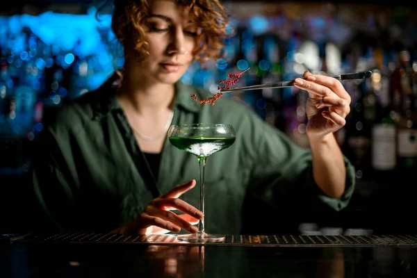 Giovane donna barista tiene il vetro con cocktail e lo decora — Foto Stock