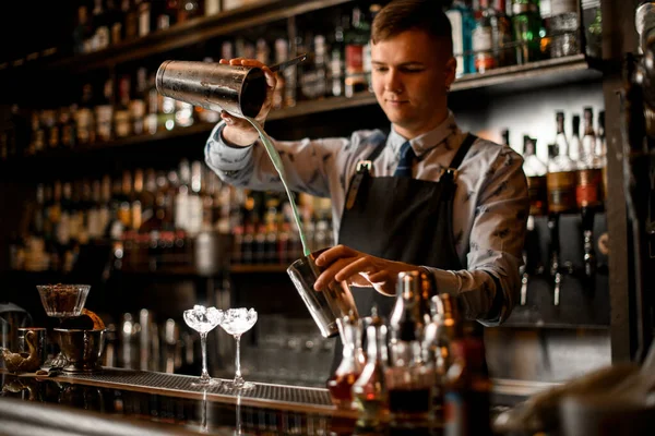 Молодий бармен п'є коктейль у шейкері. Два келихи з крижаною підставкою на барі . — стокове фото