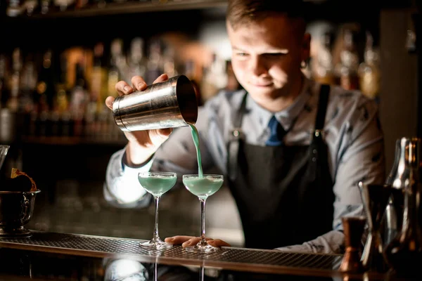 Młody barman nalewa koktajl z shakera do szklanki. — Zdjęcie stockowe