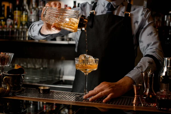 Ammattimainen baarimikko kaataa valmiiksi cocktailin lasisesta ravistimesta lasiin jäällä . — kuvapankkivalokuva