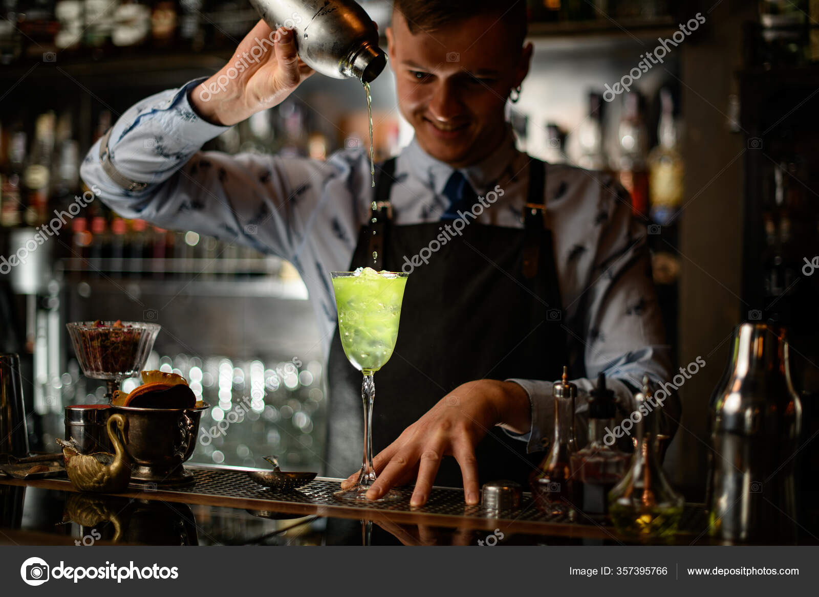 Young smiling barman pours cocktail from shaker into glass with ice. Stock  Photo by ©Fesenko 357395766