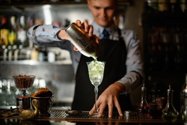 Genç barmen profesyonelce karıştırıcıdan bardağa buz dolduruyor..