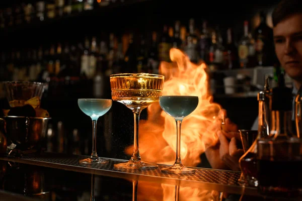 Several wineglasses stands at bar and bartender spraying and sets fire. — Stock Photo, Image