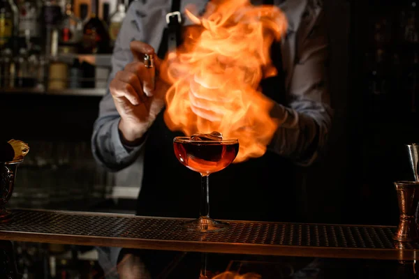 Bartender spray and burn cold brown alcoholic drink in wineglass. — Stock Photo, Image