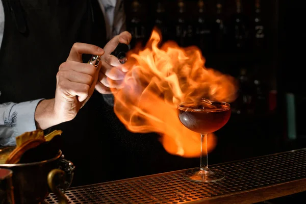 Bartender professionally spray and burn cold brown alcoholic drink in wineglass. — Stock Photo, Image