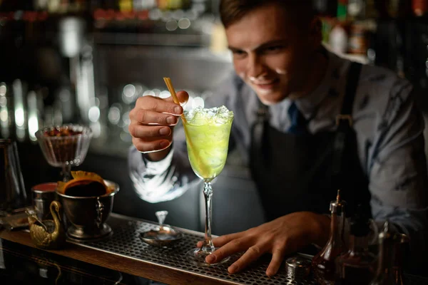 Joven barman sonriente decora por palillos de vino con cóctel verde . — Foto de Stock