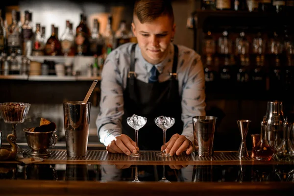 Bartendern håller två glas med is på bardisken. — Stockfoto