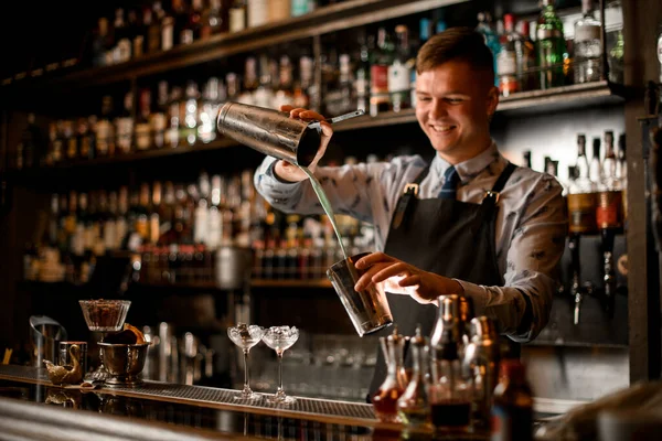 Mladý usměvavý barman nalévá koktejl do koktejlu. Dvě sklenice s ledovým stojanem na tyči. — Stock fotografie