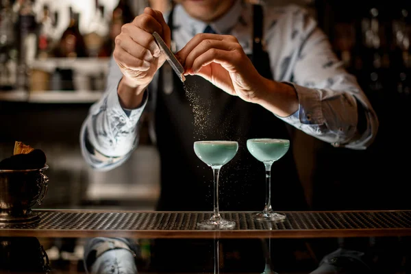 Bartender i svart förkläde dekorerar cocktail med riven mandel — Stockfoto