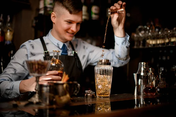 Joven camarero sonriente en el bar vierte beber en la coctelera utilizando vaso de precipitados — Foto de Stock