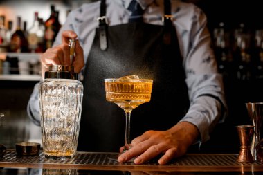Siyah önlüklü barmen dikkatle cama kahverengi alkollü kokteyl serpiyor..