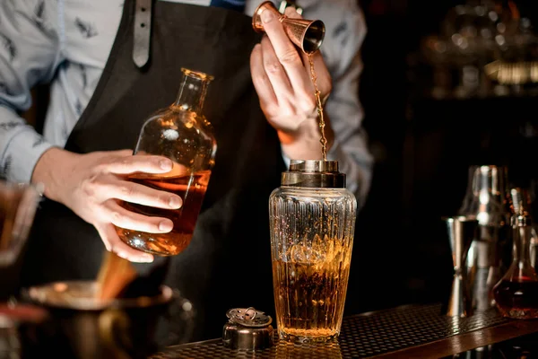 Close-up de coqueteleira vítrea em que o bartender derrama bebida usando copo . — Fotografia de Stock