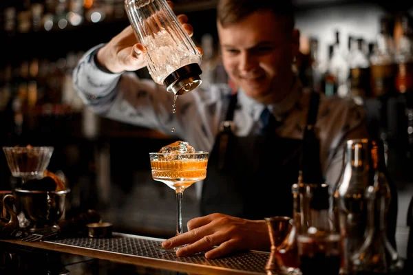 Junger lächelnder Barkeeper gießt Getränk aus Shaker ins Glas. — Stockfoto