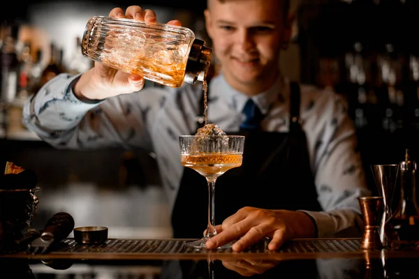 Ung leende bartender professionellt häller dryck från shaker i glas. — Stockfoto