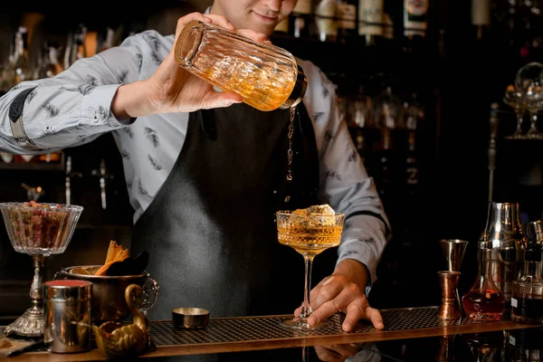 Bartender i svart förkläde häller dryck från shaker i glas. — Stockfoto