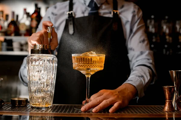 Bartender i svart förkläde strör försiktigt på glas med brun alkoholhaltig cocktail. — Stockfoto