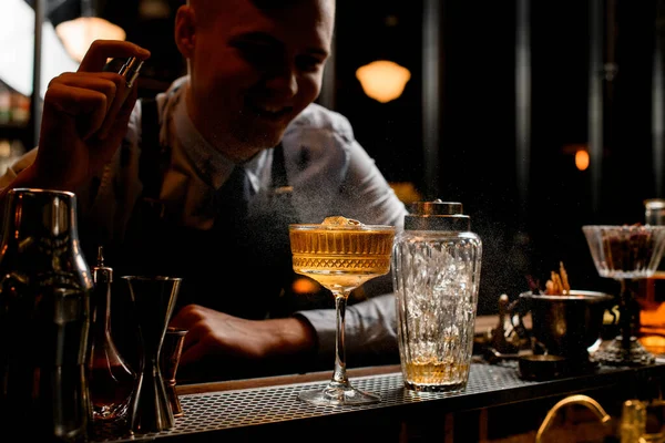 Jong glimlachend barman hagelslag op glas met ijs alcoholische drank — Stockfoto