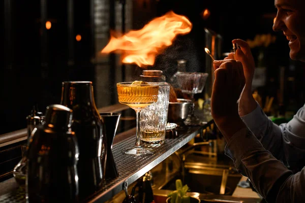 Young bartender makes fire over glass with cocktail — Stock Photo, Image