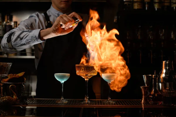 Μπάρμαν κάνει φωτιά πάνω από πολλά ποτήρια με κοκτέιλ — Φωτογραφία Αρχείου